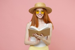 Young smart intelligent redhead cute smiling student woman 20s ginger wear straw hat glasses summer clothes holding reading interesting book isolated on pastel pink color background studio portrait