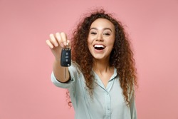 Young black african american fun smiling satisfied happy curly female driver woman 20s wear casual blue shirt giving showing close up car key isolated on pastel pink color background studio portrait