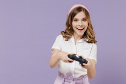 Little excited joyful fun happy smiling kid girl 12-13 years old in white shirt play pc game with joystick console isolated on purple background children studio portrait Childhood lifestyle concept