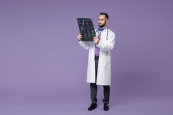 Full length of young bearded doctor man in medical gown hold x-ray brain by radiographic image ct scan mri isolated on violet background studio portrait. Healthcare personnel health medicine concept