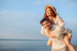Young smiling happy couple two friends family man woman in white clothes boyfriend give piggyback ride to joyful, girlfriend sit on back at sunrise over sea beach ocean outdoor seaside in summer day