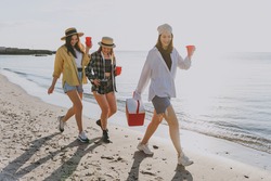 Full length female friends young women in straw hat summer clothes hang out together carry food in picnic refrigerator cups walking go outdoor on sea beach background People vacation journey concept