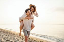 Young excited couple two friends family man woman in casual clothes boyfriend give piggyback ride to joyful girlfriend sit on back at sunrise over sea beach ocean outdoor seaside in summer day evening
