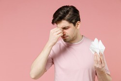 Sick ill allergic man has red eyes put hand on runny inflammation nose suffer from allergy symptoms hold paper napkin reacts on environmental allergen isolated on pastel pink color background studio