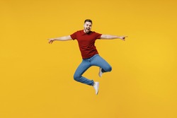 Full length overjoyed fun happy young man wear red t-shirt casual clothes jump high with outstretched hands isolated on plain yellow color wall background studio portrait. People lifestyle concept.