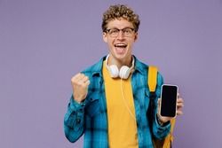 Young boy teen student in casual clothes backpack headphones use mobile cell phone blank screen workspace area do winner gesture isolated on violet background studio Education in university concept