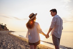 Back rear view young happy lovely couple two friends family man woman in summer clothes hold hands walking stroll together at sunrise over sea beach ocean outdoor exotic seaside in summer day evening