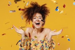 Young happy satisfied excited fun surprised amazed woman 20s with culry hair in casual clothes tossing throwing confetti isolated on plain yellow background studio portrait. People lifestyle concept