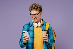 Young boy teen student in casual clothes backpack headphones glasses hold takeaway delivery cup coffee use mobile phone isolated on violet background studio Education in university college concept.