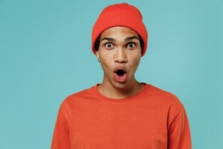 Young surprised shocked amazed african american man 20s in red shirt hat look camera with opened mouth say wow isolated on plain pastel light blue background studio portrait. People lifestyle concept