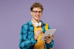 Young cool boy teen student in casual clothes backpack headphones glasses use work on tablet pc computer isolated on plain violet background studio. Education in high school university college concept