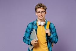 Young fun boy teen student in casual clothes backpack headphones glasses hold closed laptop pc computer isolated on plain violet background studio. Education in high school university college concept