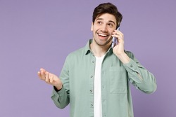 Young fun smiling happy caucasian man 20s wear casual mint shirt white t-shirt talking speaking by mobile cell phone spread hand isolated on purple background studio portrait People lifestyle concept
