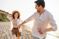 Excited lovely young couple two friends family man woman in white clothes hold hands running walk stroll dance together at sunrise over sea beach ocean outdoor seaside in summer day sunset evening.