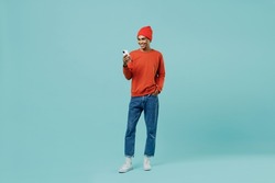 Full body young smiling happy african american man 20s in orange shirt hat use hold mobile cell phone chatting isolated on plain pastel light blue background studio portrait. People lifestyle concept