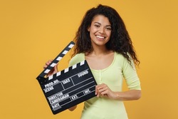 Cheerful smiling fun african american young woman 20s wears green shirt holding classic black film making clapperboard isolated on yellow background studio portrait. People emotions lifestyle concept.