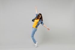 Full length side view young caucasian woman in casual denim jacket yellow t-shirt looking aside leaning back stand on toes dancing isolated on grey background studio portrait People lifestyle concept
