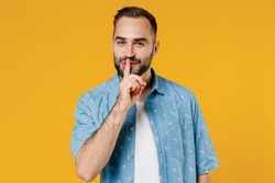 Young secret fun smiling happy caucasian man 20s wearing blue shirt say hush be quiet with finger on lips shhh gesture isolated on plain yellow background studio portrait. People lifestyle concept.