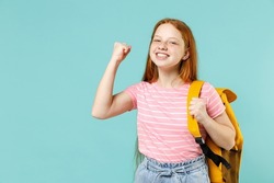 Little overjoyed pupil redhead kid girl 12-13 year old in pink t-shirt yellow school bag backpack do winner gesture clench fist isolated on pastel blue background Children lifestyle childhood concept
