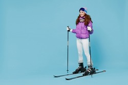 Full body skier smiling happy fun cool woman 20s wearing warm purple padded windbreaker jacket ski goggles mask spend extreme weekend in mountains look aside isolated on plain blue background studio.