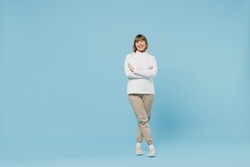 Full body size elderly cheerful caucasian smiling woman in white knitted sweater hold hands crossed folded look camera isolated on plain blue color background studio portrait. People lifestyle concept