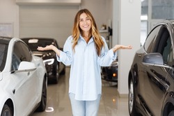 uncertain fun woman customer female buyer client wears blue shirt chooses auto between two cars wants buy new automobile in car showroom vehicle salon dealership store motor show indoor. Sales concept