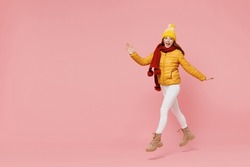 Full size body length jubilant young woman 20s years old wear yellow jacket hat mittens look camera jump move go keep mouth open hurry up isolated on plain pastel light pink background studio portrait