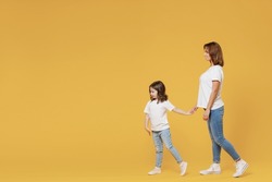 Full length happy woman in basic white t-shirt have fun child baby girl 5-6 years old hold hands walk go run Mom little kid daughter isolated on yellow color background studio Mother's Day love family