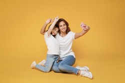 Full body length happy woman in basic white t-shirt sit on floor do selfie child baby girl 5-6 years old Mom mum little kid daughter isolated on yellow color background studio Mother's Day love family