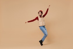 Full body young woman 20s wears red turtleneck vest beret stand on toes leaning back with outstretched hands dancing fooling around have fun isolated on plain pastel beige background studio portrait.