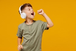 Little small happy boy 6-7 years old wearing green t-shirt headphones listen to music sing song in microphone isolated on plain yellow background studio. Mother's Day love family lifestyle concept.
