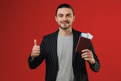 Traveler tourist latin man in black jacket grey shirt hold passport ticket show thumb up gesture isolated on red background. Passenger travel abroad on weekends getaway. Air flight journey concept.