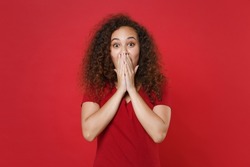 Shocked young african american woman girl in casual t-shirt posing isolated on bright red background studio portrait. People emotions lifestyle concept. Mock up copy space. Covering mouth with hands