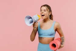 Young strong sporty fitness trainer instructor woman wear blue tracksuit spend time in home gym hold scream megaphone announces discounts sale isolated on plain pink background. Workout sport concept
