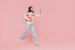 Full body teen student girl of Asian ethnicity in sweater hold backpack jump high use mobile cell phone jump high isolated on pastel plain light pink background Education in university college concept