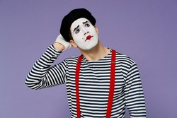 Puzzled thoughtful gloomy young mime man with white face mask wears striped shirt beret look up rub head iterates over solution options isolated on plain pastel light violet background studio portrait