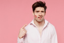 Young sad caucasian man 20s with wearing casual shirt look camera point finger on lipstick lips on face cheek isolated on pink background studio. Valentine's Day birthday holiday party dating concept.