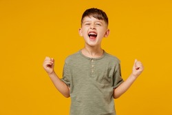 Little happy small fun happy child kid boy 6-7 years old wearing green t-shirt do winner gesture clench fist celebrate isolated on plain yellow background. Mother's Day love family lifestyle concept