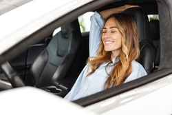 Relaxed fun happy driver woman customer buyer client in blue shirt close eyes sit in car choose auto want buy new automobile in showroom vehicle salon dealership store motor show indoor.Sales concept