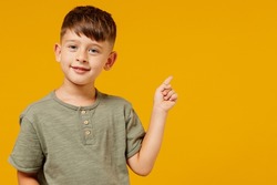 Little small happy boy 6-7 years old in green casual t-shirt point index finger aside on workspace area isolated on plain yellow background studio portrait. Mother's Day love family lifestyle concept.
