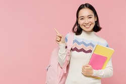 Teen student girl of Asian ethnicity wear sweater backpack hold books point index finger aside on workspace area isolated on pastel plain light pink background Education in university college concept
