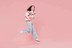 Full body side view happy teen student girl of Asian ethnicity wear sweater hold backpack books jump high run fast isolated on pastel plain pink background Education in university college concept.