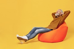 Full size body length happy elderly gray-haired bearded man 40s years old wears brown shirt hands folded under head have rest relax sit in bag chair isolated on plain yellow background studio portrait