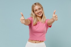 Young smiling cheerful caucasian blonde woman 20s wearing casual pink t-shirt look camera show thumb up gesture isolated on plain pastel light blue background studio portrait. People lifestyle concept