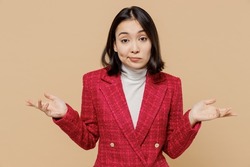 Confused woman of Asian ethnicity 20s wear red jacket shrugging shoulders looking puzzled, have no idea spread hands isolated on plain pastel beige background studio People lifestyle fashion concept