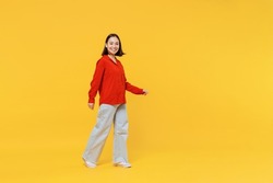 Full size body length vivid young woman of Asian ethnicity 20s years old in casual clothes look camera go move isolated on plain yellow background studio portrait. People emotions lifestyle concept