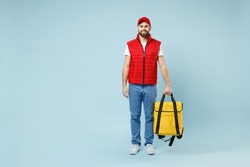Full size body length delivery guy employee man in red cap white T-shirt uniform work as courier hold yellow thermal food bag backpack isolated on pastel blue color background studio. Service concept