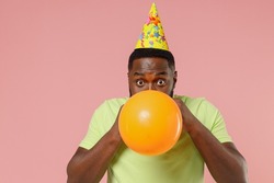 Young happy fun black guy man 20s wear green t-shirt bow tie inflates orange balloon celebrating birthday party isolated on plain pastel pink color background studio portrait. People lifestyle concept