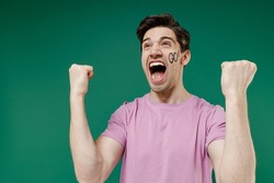 Young fun crazy happy european man fan supporter wears basic pink t-shirt cheer up support football sport team watch tv live stream scream clench fists isolated on dark green color background studio