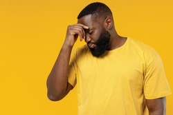 Young sad pensive minded unhappy black man 20s wearing bright casual t-shirt keep eyes closed rub put hand on nose isolated on plain yellow color background studio portrait. People lifestyle concept